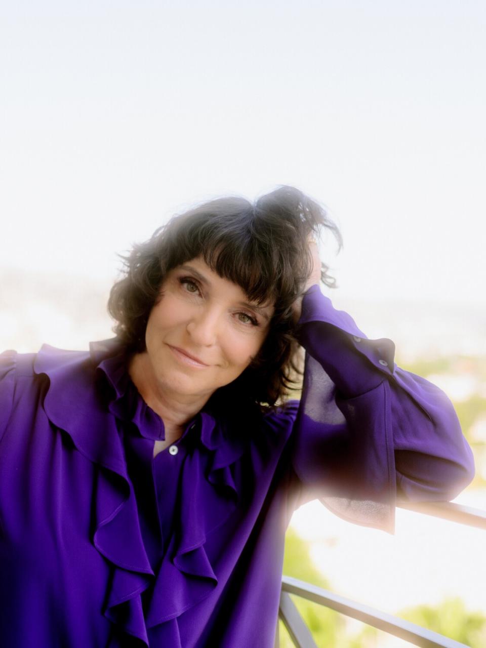 A woman in a purple shirt leans against a balcony.