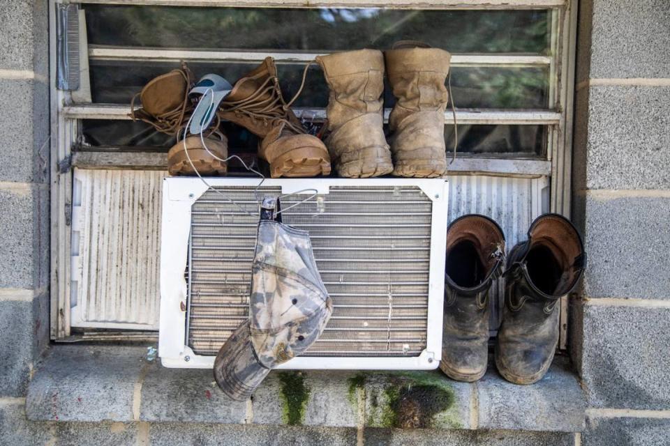 Boots and a hat dry on a window air conditioning unit at a Johnston County farmworker camp Thursday August 27, 2020. Air conditioning is considered a luxury by many farmworkers in North Carolina farmworker camps.