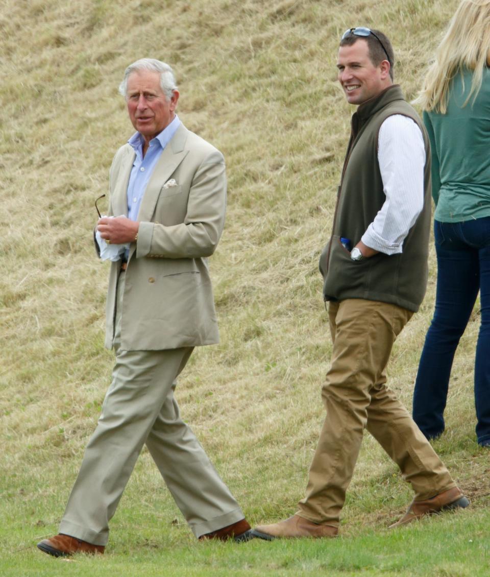 King Charles and Peter Phillips walking on a grassy hill.