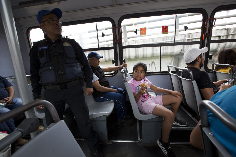 En esta fotografía del 15 de mayo de 2019, una niña se sienta cerca de un agente de la policía en la parte trasera de un camión del transporte público, en la Ciudad de México. (AP Foto/Rebecca Blackwell)