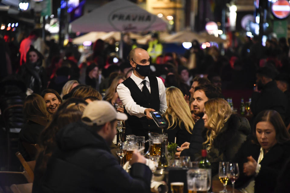 FILE - In this Wednesday, Nov. 4, 2020 file photo, a waiter wears a face mask as people eat and drink outside restaurants in Soho, in London. British Prime Minister Boris Johnson is expected to confirm Monday June 14, 2021, that the next planned relaxation of coronavirus restrictions in England will be delayed as a result of the spread of the delta variant first identified in India. (AP Photo/Alberto Pezzali, File)