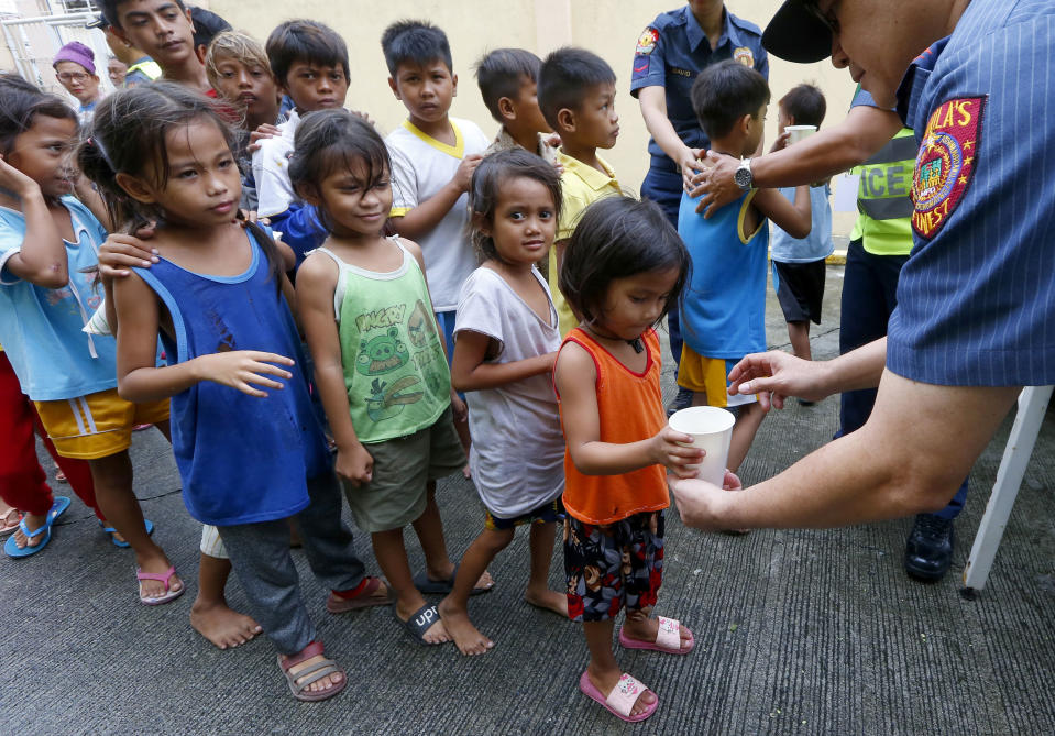 FILE - In this Saturday, Sept. 15, 2018, file photo, Manila police give out rice porridge to residents living along the coastal community of Baseco as they evacuate during the onslaught of Typhoon Mangkhut which barreled into the northeastern Philippines before dawn in Manila, Philippines. (AP Photo/Bullit Marquez, File)