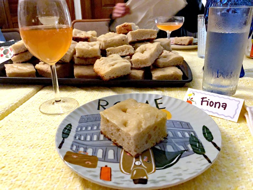 piece of focaccia bread bread on a plate with a wine glass and a tray of bread on the table behind it