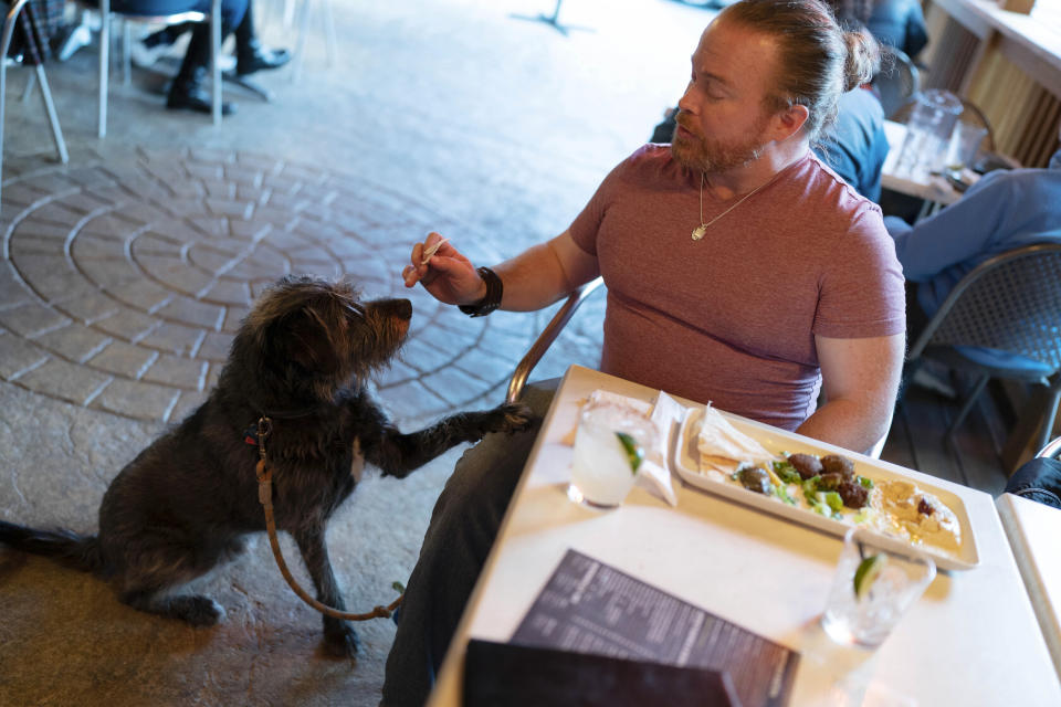Monty Hobbs shares food with his dog Mattox on the patio at the Olive Lounge in Takoma Park, Md., on Thursday, May 4, 2023. Just in time for the summer dining season, the U.S. government has given its blessing to restaurants that want to allow pet dogs in their outdoor spaces. (AP Photo/Jose Luis Magana)