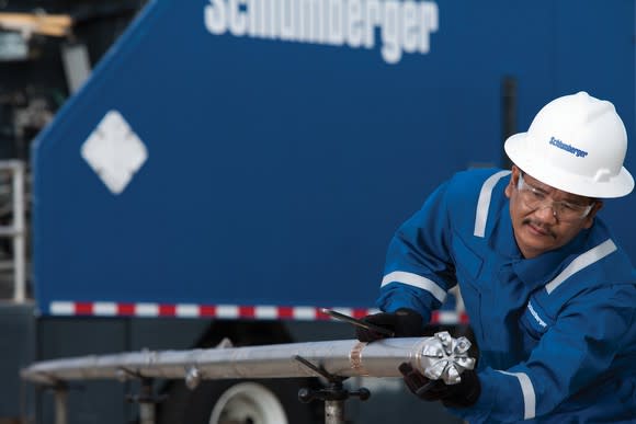 Person wearing Schlumberger hard hat holding a drill bit in front of a trailer.