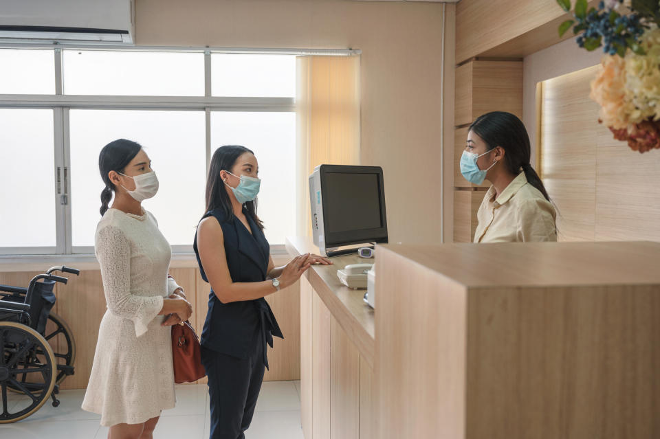Patients wearing face mask contact for treatment sickness with receptionist at counter reception in hospital