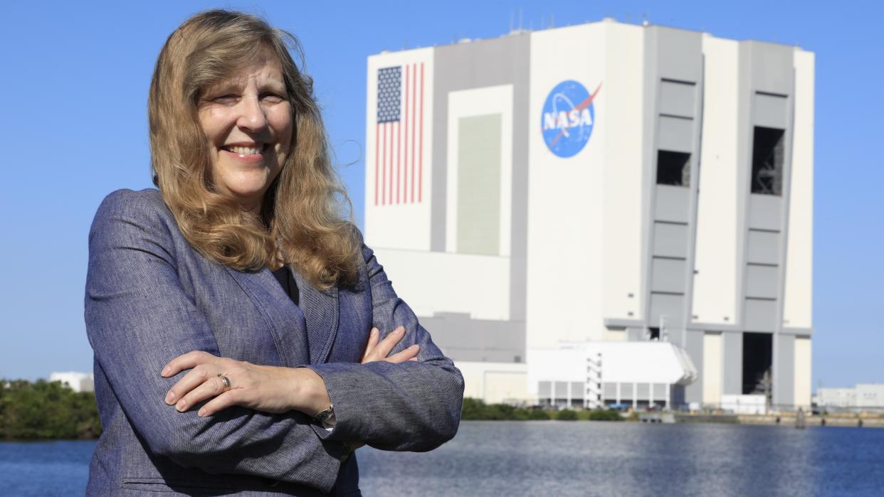  Woman standing in front of big square building with nasa logo and american flag. 