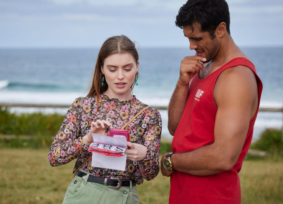 Chloe shows Tane some information she's found, with Palm Beach in the background