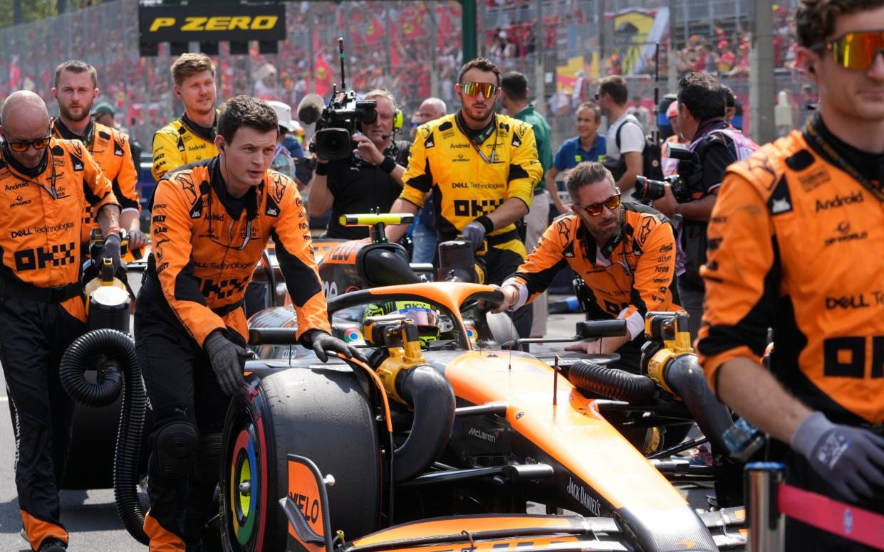 The McLaren mechanics wheel Lando Norris' car onto the grid