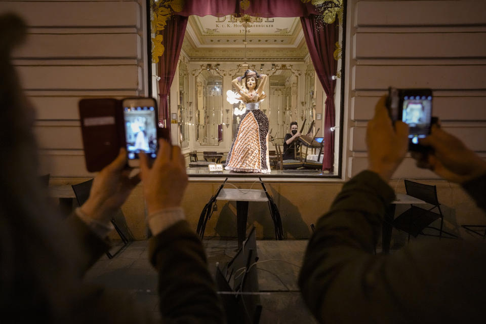 People take pictures as a sweets shop employee handles furniture after closing time in Vienna, Austria, Saturday, Nov. 20, 2021. The Austrian government announced a nationwide lockdown that will start Monday and comes as average daily deaths have tripled in recent weeks and hospitals in heavily hit states have warned that intensive care units are reaching capacity. (AP Photo/Vadim Ghirda)