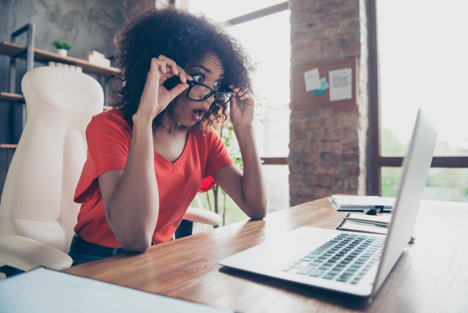 Surprised woman in orange top looking over her glasses at laptop screen