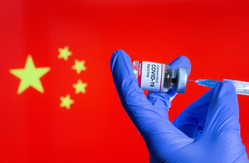 FILE PHOTO: A woman holds a small bottle labeled with a "Coronavirus COVID-19 Vaccine" sticker and a medical syringe in front of displayed China flag in this illustration