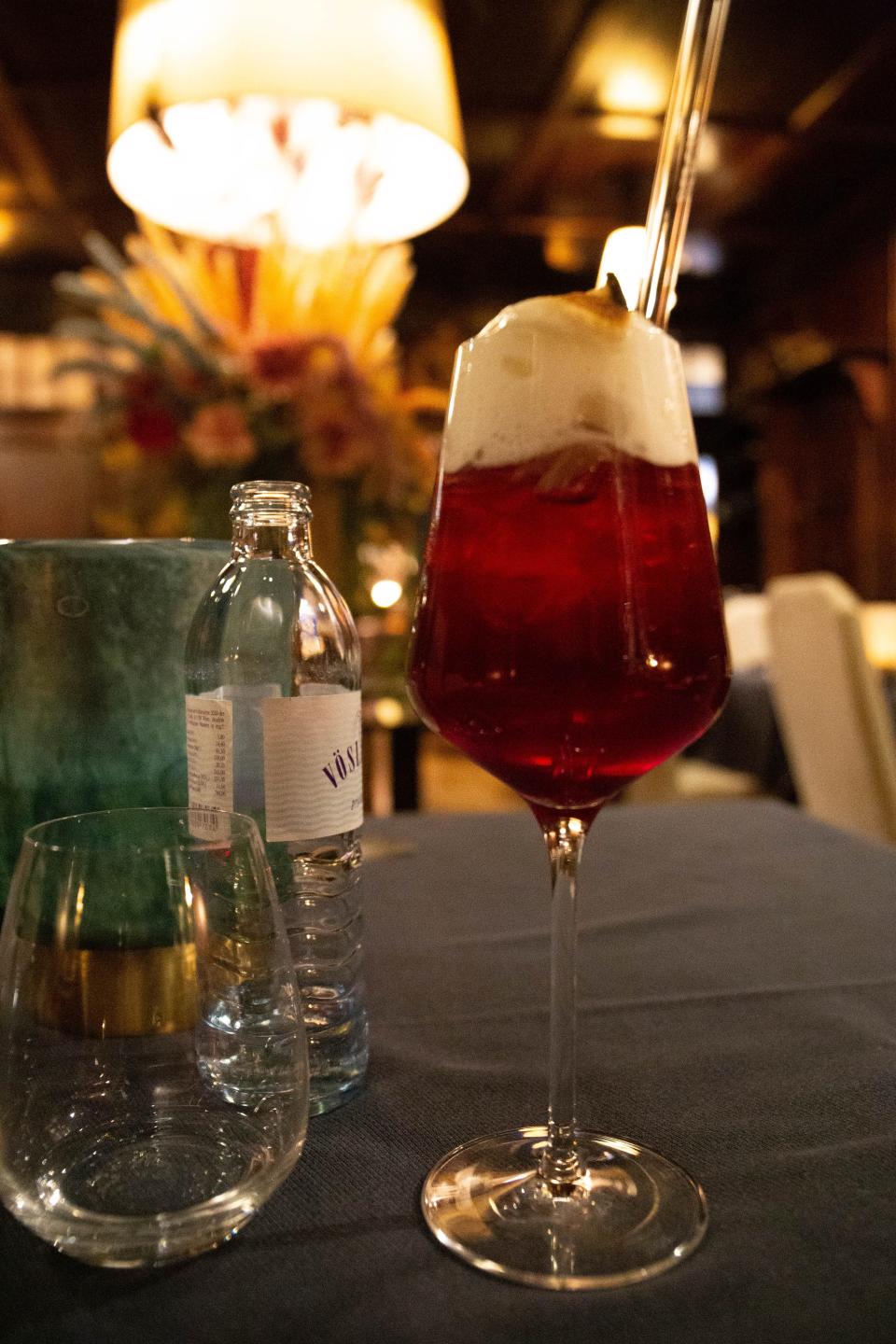 Photo of a red cocktail in a tall wine glass with a glass straw