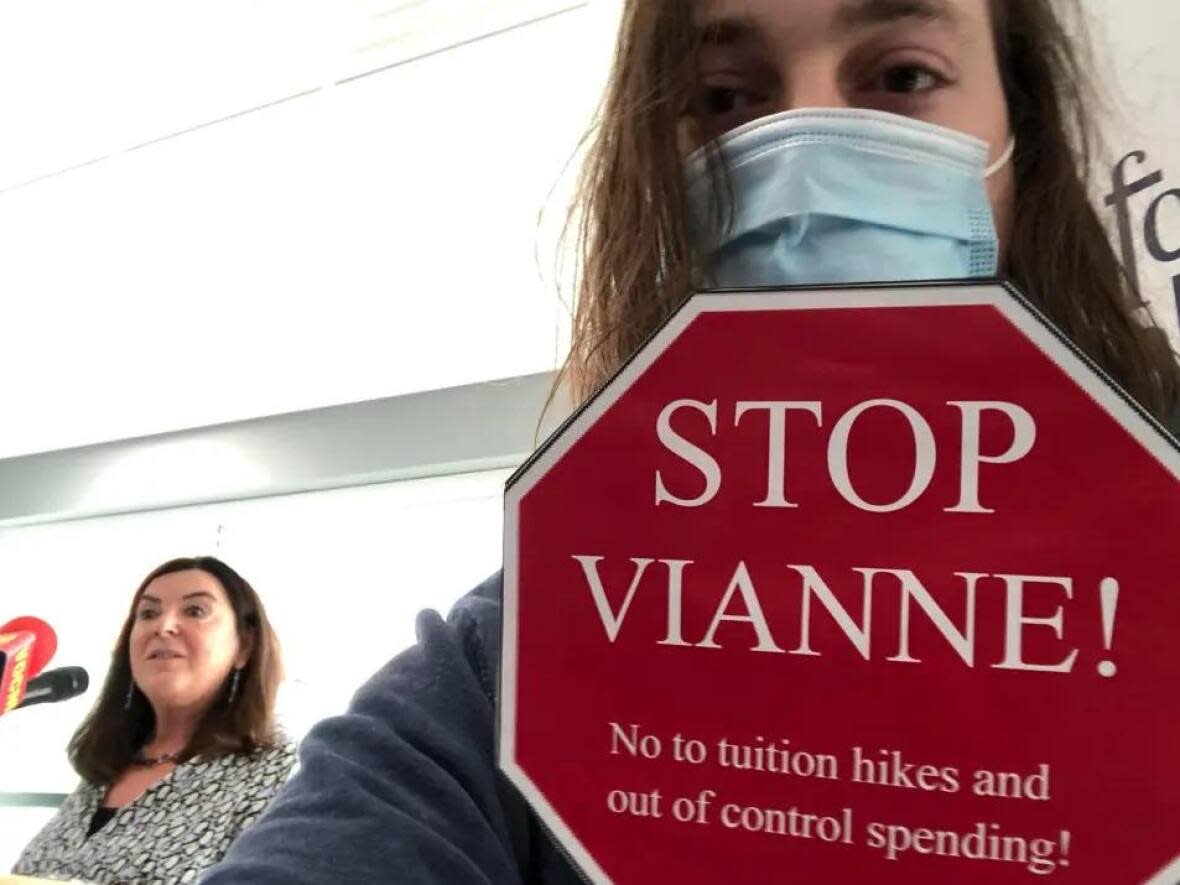 Matt Barter holds up a sign criticizing Memorial University president Vianne Timmons, left, as she speaks at a media briefing Thursday, Dec. 2, 2021. (Submitted by Matt Barter - image credit)