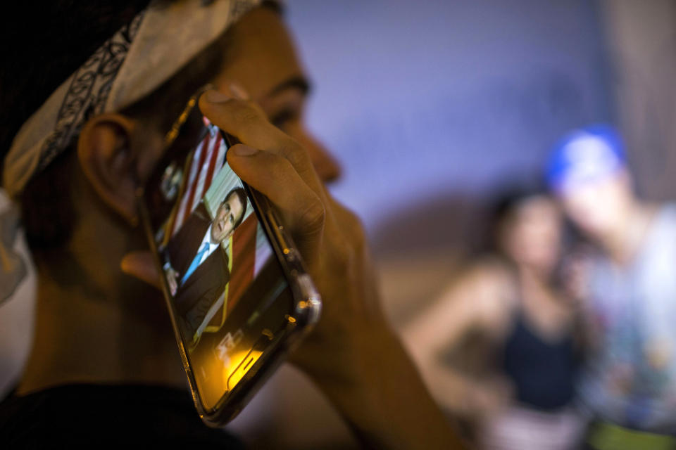 Locals listen on a smart phone to the pre-recorded message by Puerto Rico Gov. Ricardo Rossello announcing that he is resigning Aug. 2 after nearly two weeks of protests and political upheaval touched off by a leak of crude and insulting chat messages between him and his top advisers in San Juan, Puerto Rico, Wednesday, July 24, 2019. (AP Photo/Dennis M. Rivera Pichardo)