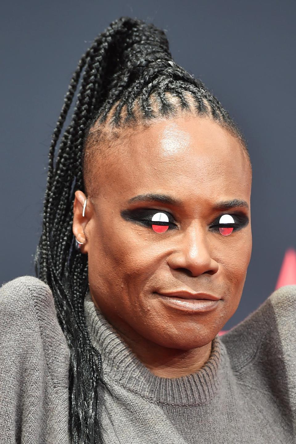 Billy in a soft outfit poses on the red carpet with braided hair and dramatic makeup