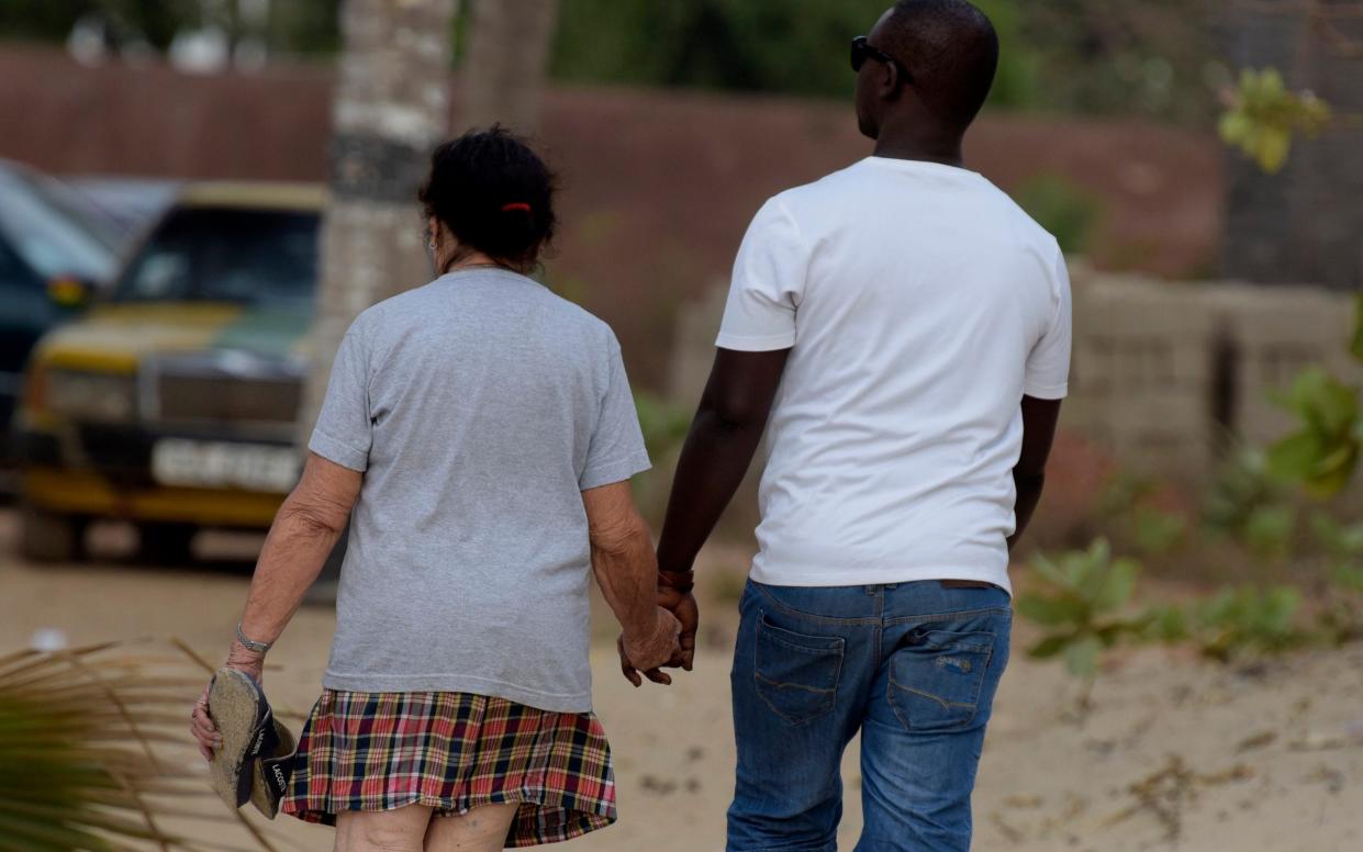 A woman and a young man walk hand in hand along a beach - Seyllou/AFP via Getty Images