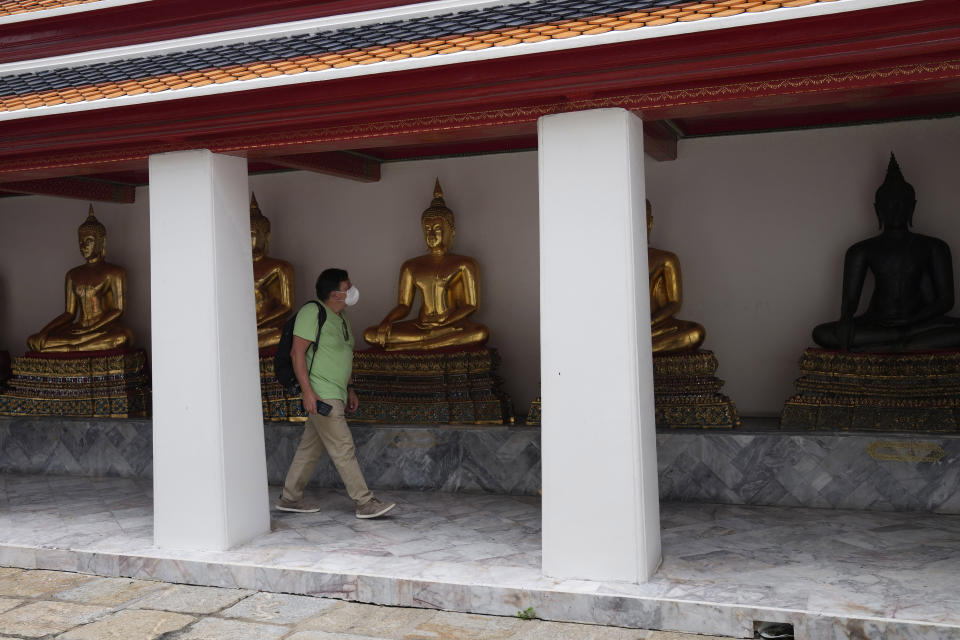 A tourist wearing protective masks tours at Wat Pho temple in Bangkok, Thailand, Wednesday, Feb. 23, 2022. Thailand will ease some entry requirements for foreign visitors as it balances a rising number of coronavirus cases with the need to rebuild its pandemic-damaged economy, the government announced Wednesday. (AP Photo/Sakchai Lalit)