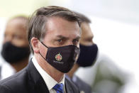 FILE - In this May 18, 2020, file photo, Brazilian President Jair Bolsonaro wears a mask due to the coronavirus pandemic as he talks with supporters upon departure from his official residence, Alvorada palace, in Brasilia, Brazil. The logo on the mask reads "Military Police. Federal District." After 35 years of civilian-led democracy, Bolsonaro has created the most militarized Brazilian government since the fall of the country’s army-led dictatorship. (AP Photo/Eraldo Peres, File)