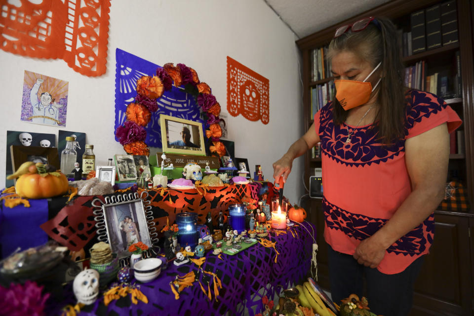 Rosario Martinez, lights candles on a Day of the Dead altar for her husband Dr. Jose Luis Linares, who died from symptoms related to COVID-19, at their home in Mexico City, Sunday, Nov. 1, 2020. He is one of more than 1,700 Mexican health workers officially known to have died of COVID-19 who are behind honored with three days of national mourning on these Days of the Dead. (AP Photo/Eduardo Verdugo)