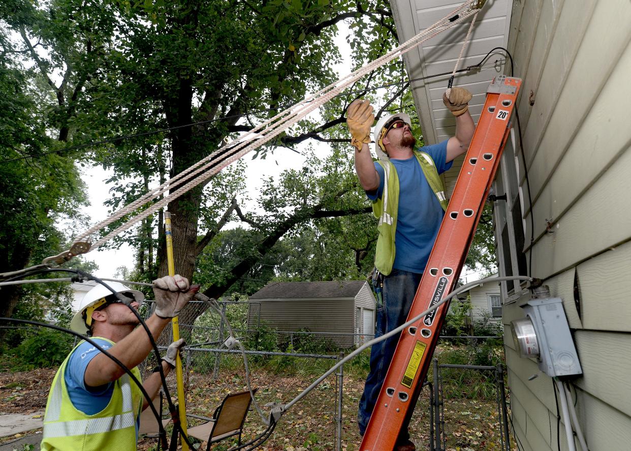 Paul Cummings, right, and Scott Franklin of City Water, Light and Power reattach a power line onto a house on South Ninth Street Friday, June 30, 2023. They were part of a crew out recording damage locations and fixing what they could from the derecho storm that struck June 29.