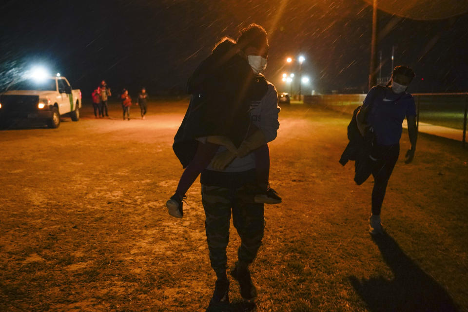 A migrant carries a child at an intake area after turning themselves in upon crossing the U.S.-Mexico border, late Tuesday, May 11, 2021, in La Joya, Texas. The U.S. government continues to report large numbers of migrants crossing the U.S.-Mexico border with an increase in adult crossers. But families and unaccompanied children are still arriving in dramatic numbers despite the weather changing in the Rio Grande Valley registering hotter days and nights. (AP Photo/Gregory Bull)