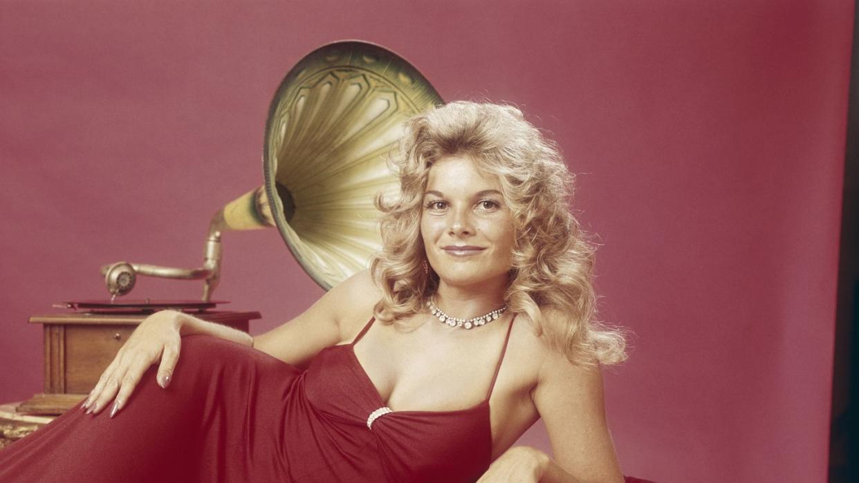 Young woman leaning on cushion with gramophone in background, smiling, portrait