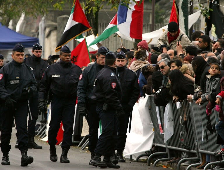Policemen walk past the people gathered outside the Percy military hospital in the Paris southwestern suburb of Clamart, November 11, 2004, after Yassser Arafat died overnight at the age of 75