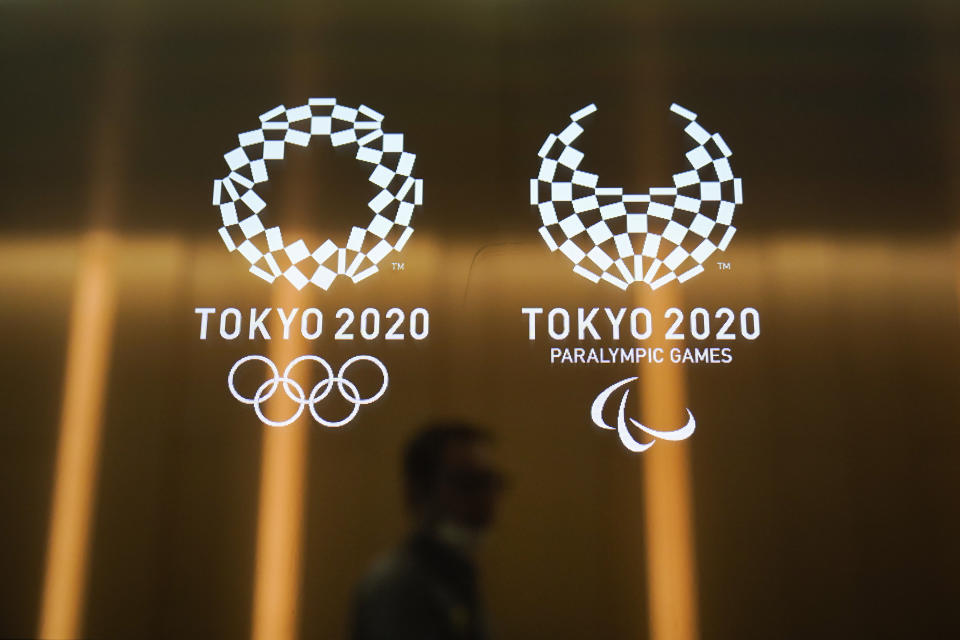 FILE - In this June 11, 2019, file photo, a man walks past the Tokyo 2020 Olympic logos, in Tokyo. Tokyo is building eight new venues. The other 35 venues are defined as “temporary” or older buildings being reused. (AP Photo/Jae C. Hong, File)