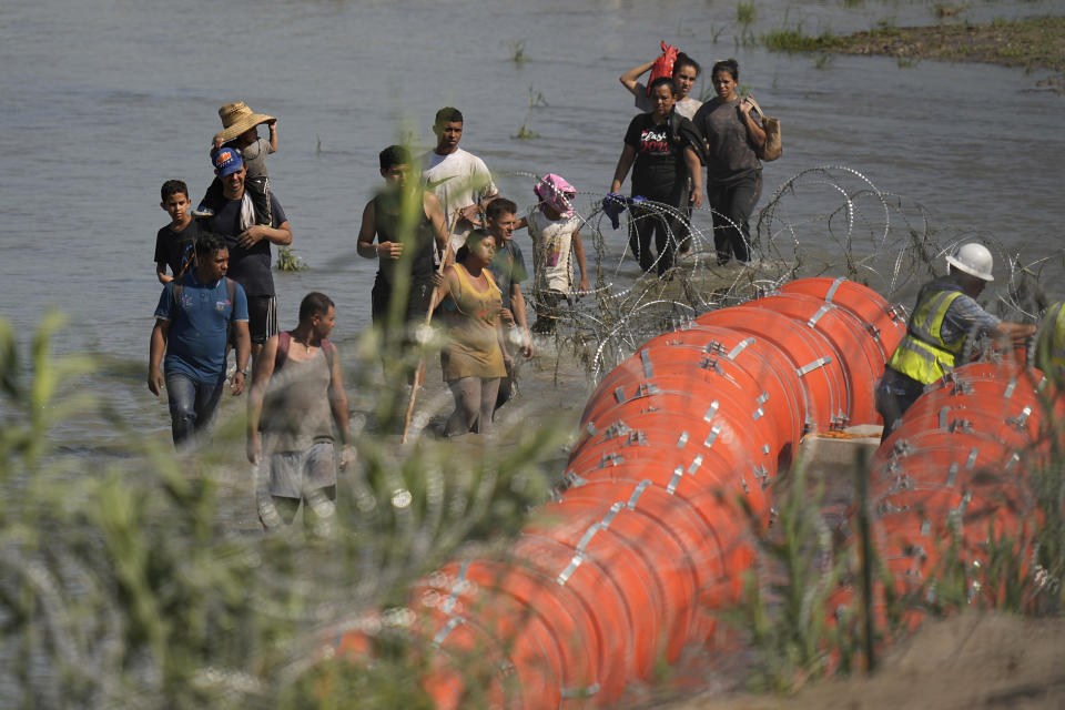 Migrants trying to enter the U.S. from Mexico approach the site where workers are assembling large buoys to be used as a border barrier along the banks of the Rio Grande near Eagle Pass , Texas, Tuesday, July 11, 2023. The floating barrier is being deployed in an effort to block migrants from entering Texas from Mexico. (AP Photo/Eric Gay)