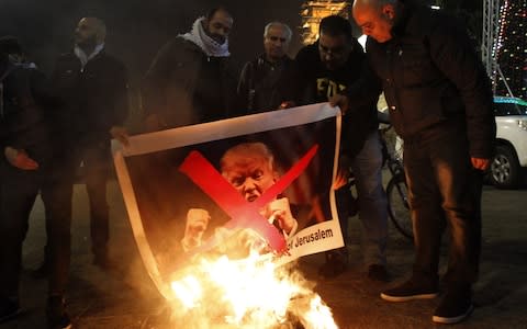 Palestinian protesters burn pictures of US President Donald Trump at the manger square in Bethlehem on Tuesday  - Credit: MUSA AL SHAER /AFP