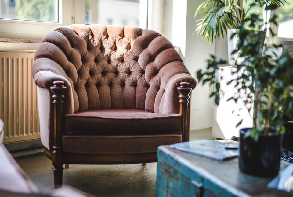 Sunny relaxation area with old-fashioned upholstered armchair and trunk in eclectically decorated office.