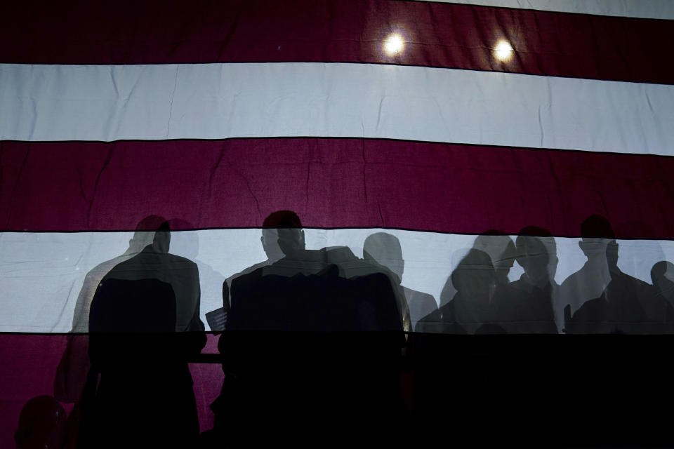 FILE - Silhouettes of people are seen on an American flag as President Joe Biden speaks at Max S. Hayes Hight School, Wednesday, July 6, 2022, in Cleveland. Conspiracy theories are nothing new. Humans have always speculated about secret motives and plots as a way to understand their world and avoid danger. But these days, conspiracy theories and those who believe them seem to be playing an outsized role in our politics and culture. (AP Photo/Evan Vucci, File)