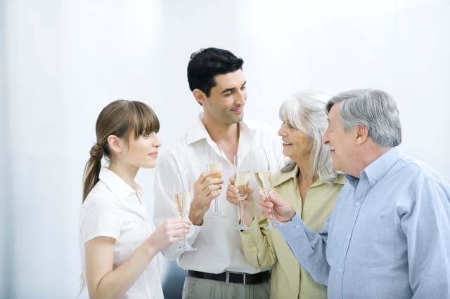 B4A07M Couple standing with senior parents, all holding champagne flutes