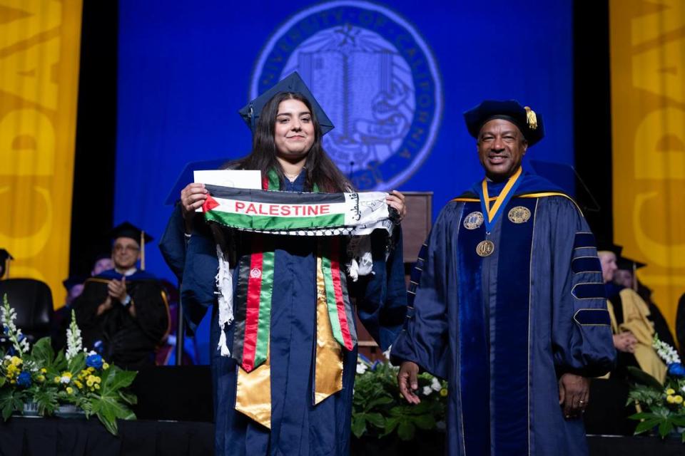 Nahila Habib, graduating with a bachelor’s degree in human development and a minor in biological psychology, holds up a Palestine banner as she stands next to UC Davis Chancellor Gary May while crossing the stage to receive her diploma on Friday.