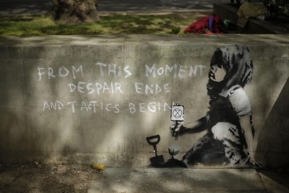 Dappled shade from a tree is cast over a new piece of street art that people noticed for the first time last night and is believed to be by street artist Banksy on a wall where Extinction Rebellion climate protesters had set up a camp in Marble Arch, London, Friday, April 26, 2019. Extinction Rebellion ended its remaining blockades in London on Thursday evening with a closing ceremony, after disrupting the British capital for 10 days. The non-violent protest group is seeking negotiations with the government on its demand to make slowing climate change a top priority. (AP Photo/Matt Dunham)