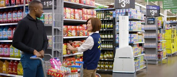 A Wal-Mart employee talks with a customer with a Bossa Nova robot scanning the next aisle.