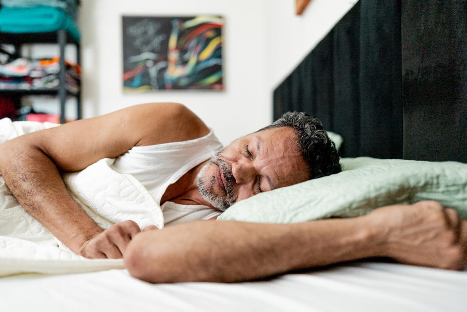 Man sleeping on his side in a bed with a green pillow in a room with a piece of abstract art on the wall