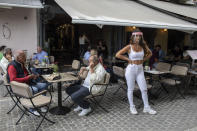 A cafe-restaurant staff stands outside as people drink coffee in Monastiraki district of Athens, on Monday, May 25, 2020. Greece restarted regular ferry services to its islands Monday, and cafes and restaurants were also back open for business as the country accelerated efforts to salvage its tourism season. (AP Photo/Petros Giannakouris)