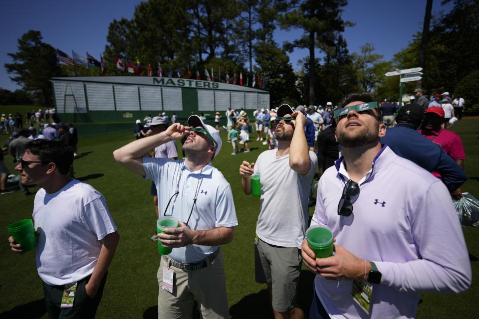 Patrons look up at the sun during an solar eclipse during a practice round in preparation for the Masters golf tournament at Augusta National Golf Club Monday, April 8, 2024, in Augusta, Ga. (AP Photo/Matt Slocum)
