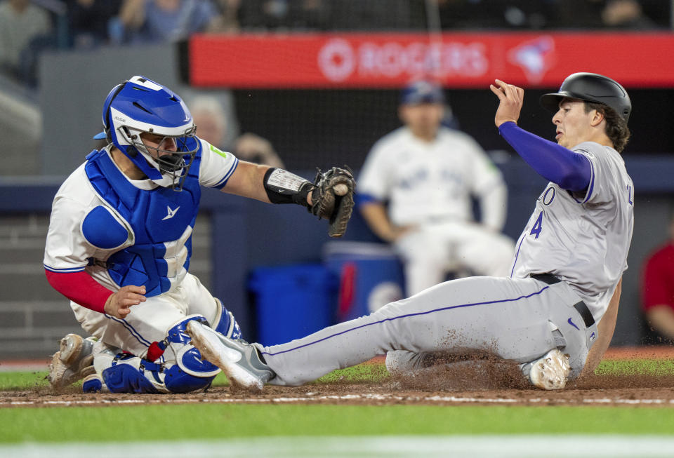 Colorado Rockies'r Michael Toglia (4) slides in to score under a tag by Toronto Blue Jays catcher Alejandro Kirk during seventh-inning baseball game action in Toronto, Friday, April 12, 2024. (Frank Gunn/The Canadian Press via AP)