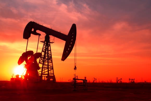 A silhouette of an oil pump in an oil field at sunset.