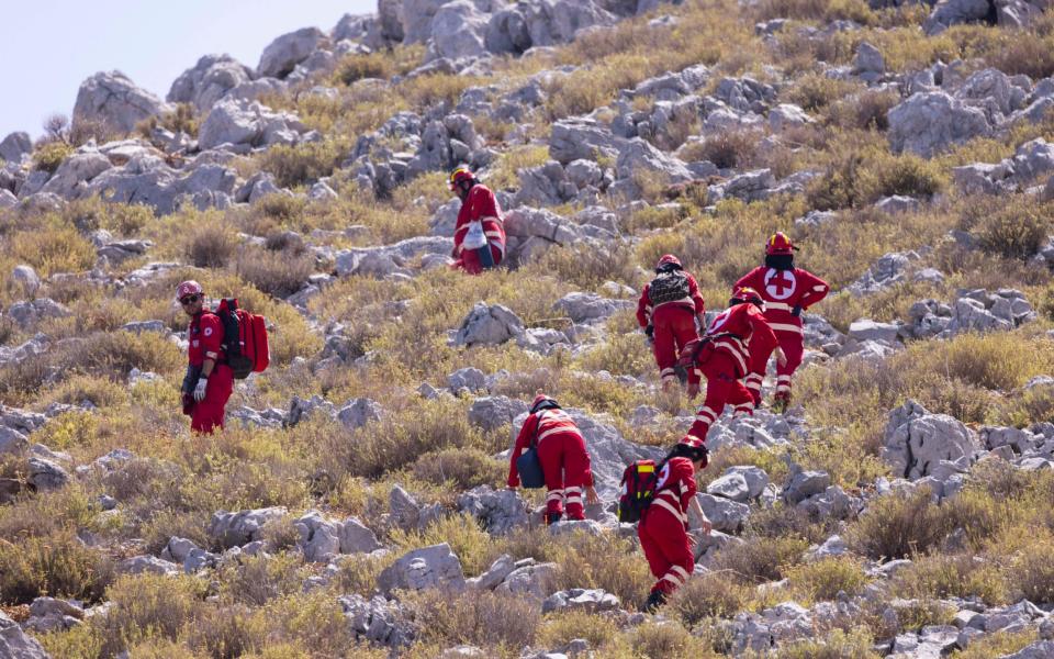 Red Cross workers in red uniforms search a barren hillside