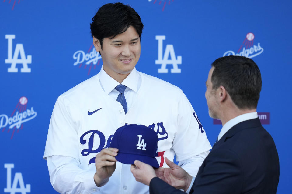 Los Angeles Dodgers' Shohei Ohtani, left, is handed a baseball cap by president of baseball operations Andrew Friedman during a news conference at Dodger Stadium Thursday, Dec. 14, 2023, in Los Angeles. (AP Photo/Ashley Landis)