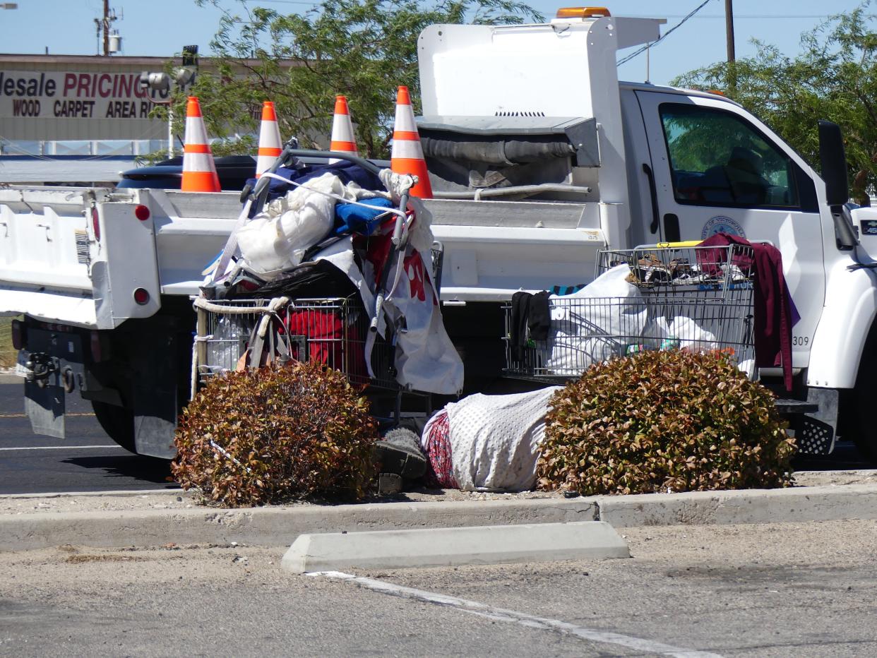 A homeless woman sleeps alongside her belongings near a sidewalk on Seventh Street in Victorville.