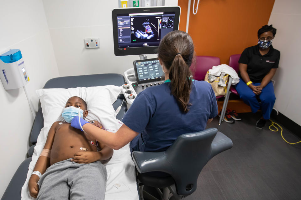 Recovering from MIS-C, Xavier Gardner gets an echocardiogram from sonographer Chasity Robertson as his mother, Cheryl Gardner, looks on.