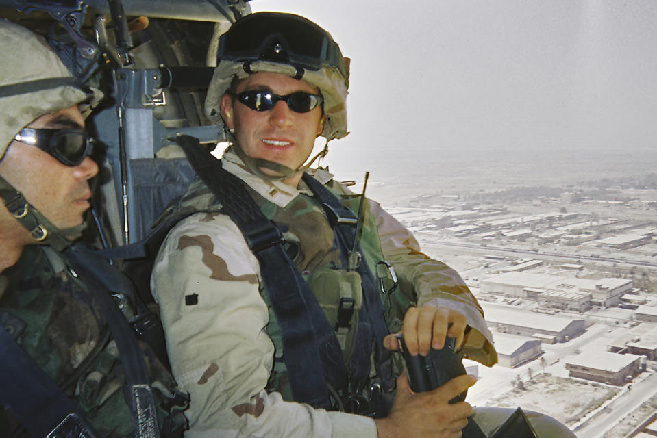 In this image provided by Rep. Jason Crow, Army Lt. Jason Crow sits in a helicopter as he flies over Baghdad in 2003. Two decades ago, Crow was a 24-year-old platoon leader in the American invasion of Iraq. Platoon members carried gas masks and gear to wear over their uniforms to protect them from the chemical weapons the U.S. believed – wrongly – that Iraqi forces might use against them. (Rep. Jason Crow via AP)