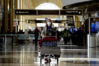 A woman wearing a mask walks through a terminal at Ronald Reagan Washington National Airport, Monday, March 16, 2020, in Arlington, Va. (AP Photo/Andrew Harnik)
