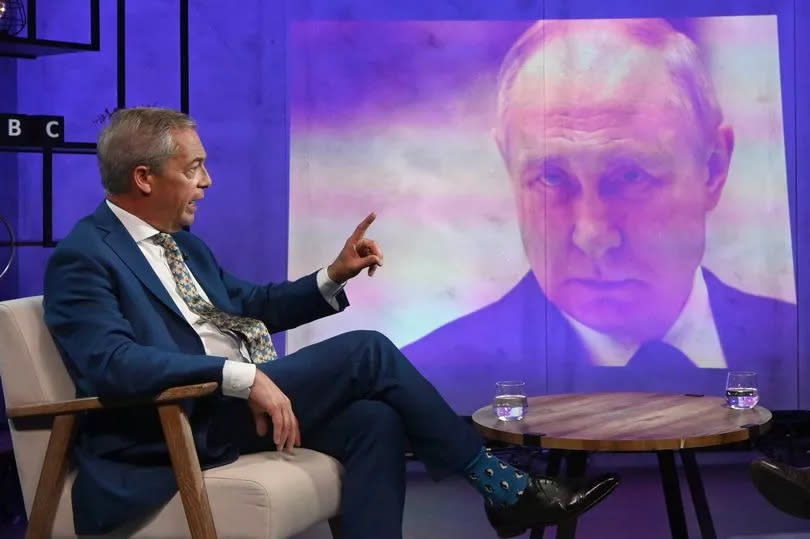 Nigel Farage points a finger with a picture of Vladimir Putin in the background