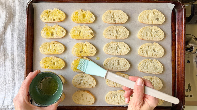 Brushing olive oil on baguette slices on parchment-lined baking sheet